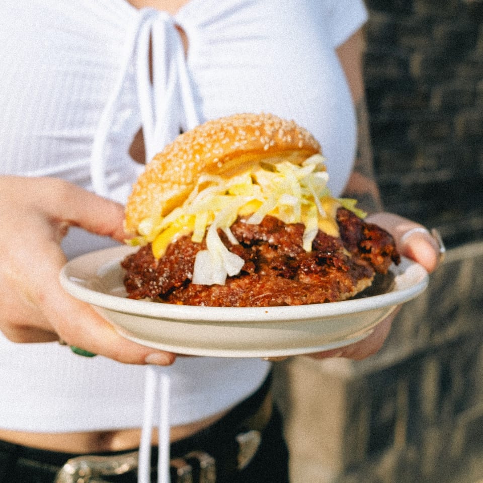 Hands holding a plate with a large burger topped with chili, cheese, and shredded lettuce.